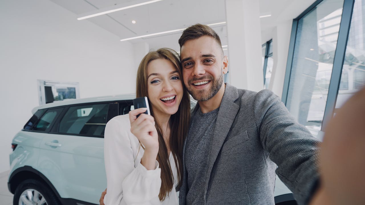 A joyful couple taking a selfie after purchasing a new car, indoors.