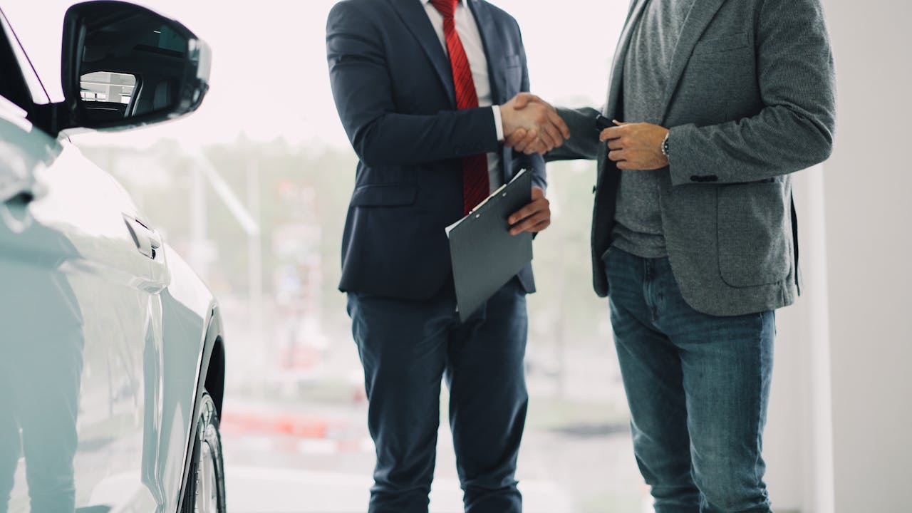 Two men shake hands in a car dealership, sealing a business deal.