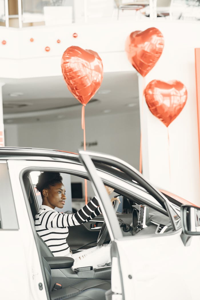 A woman in a car surrounded by heart-shaped balloons, expressing celebration and joy.